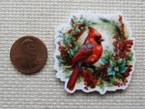 Minder of a red cardinal bird with berries next to a penny for scale on a textured surface