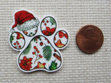 Decorative paw print minder with Christmas-themed designs next to a penny for scale on a textured surface.