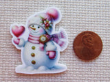 Decorative snowman minder with hearts next to a penny on a textured surface