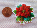 Minder of a red poinsettia flower next to a penny on a textured surface