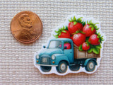 Minder of a blue truck with strawberries next to a penny on a textured surface