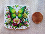 Decorative minder with a green butterfly and flowers next to a penny on a textured surface