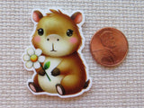 Minder of a cute capybara holding a flower next to a penny on a textured surface