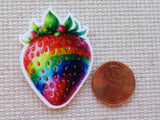 Colorful strawberry-shaped minder next to a penny on a textured surface