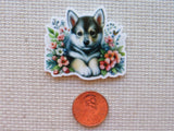 Minder of a puppy surrounded by flowers on a textured surface with a penny for scale.