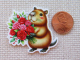 Minder of a capybara holding flowers next to a penny for scale on a textured surface
