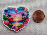 Heart-shaped tropical scene minder next to a penny on a textured surface
