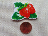 Minder of a strawberry with green leaves next to a penny on a textured surface