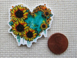 Heart-shaped minder with sunflower design next to a penny on a textured surface