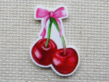 Minder of two cherries with a pink bow on a textured beige background
