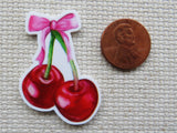 Minder of cherries with a pink bow next to a penny on a textured surface