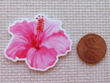 Pink flower minder next to a penny on a textured surface