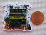 Halloween-themed minder with books and pumpkins next to a penny for scale on a textured surface.