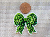 Green floral bow minder next to a penny on a textured fabric background