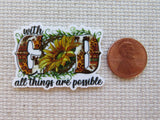 Minder with sunflower design and 'with God all things are possible' text next to a penny on a textured surface