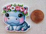 Cute cartoon hippo minder with floral crown next to a penny for scale on a textured background
