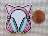 Minder with pink and blue headphones and cat ears next to a penny on a textured surface