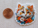 Minder of a cat with floral design next to a penny on a textured surface