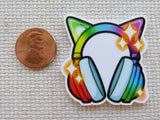 Colorful cat-shaped minder with headphones next to a penny for scale on a textured surface