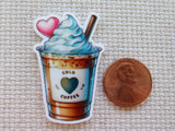 Minder of a cold coffee with whipped cream and a heart, next to a penny for scale.