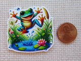 Colorful frog minder on a textured surface with a penny for scale.