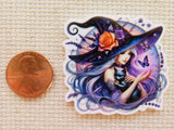Minder of a witch with purple hair and a purple hat next to a penny on a textured surface