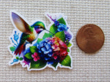 Colorful minder of a hummingbird and flowers next to a penny on a textured surface