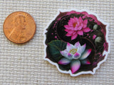 Minder of pink lotus flowers next to a penny on a textured fabric background