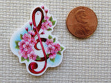 Decorative minder with floral design and red treble clef next to a penny for scale on a textured fabric background
