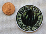 Minder with 'Bigfoot Research Team' design next to a penny on a textured surface