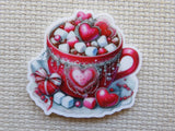 Decorative minder of a red cup with heart designs and candy on a textured surface
