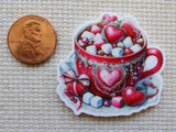 Decorative minder of a red mug with heart designs and candy next to a penny for scale.