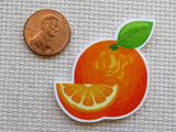 Minder of an orange with a slice next to a penny for scale on a textured surface