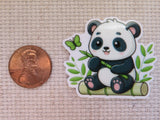 Minder featuring a cute cartoon panda holding bamboo, placed next to a US penny on a textured beige fabric background.