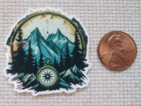 Minder with mountain and compass design next to a penny on a textured surface