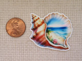 Colorful shell-shaped minder with a scenic design next to a penny on a textured fabric background