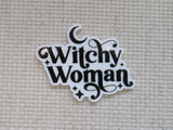 A minder with the phrase 'Witchy Woman' in black decorative lettering on a white background, placed on a beige woven fabric surface.