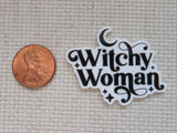 A minder with the words 'Witchy Woman' in black script on a white background, shown next to a copper penny for scale on a beige woven fabric background.