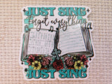 A minder featuring the text 'JUST SING Forget everything' with an illustration of an open songbook, musical notes, and colorful flowers, shown on a beige woven fabric background.
