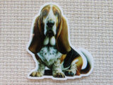 A minder of a Basset Hound dog sitting down, displayed on a textured beige woven fabric background.
