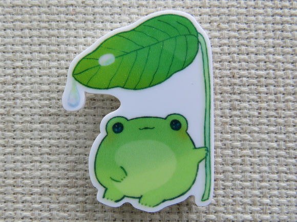First view of a frog  sitting under a leaf with a couple of raindrops on it needle minder.
