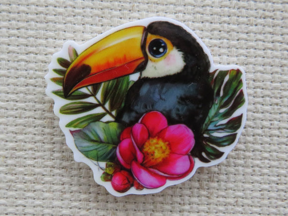 First view of a toucan sitting in leaves with a flower minder.