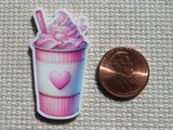 A minder of a pink soft-ice drink in a striped cup with a heart emblem, shown next to a U.S. penny.