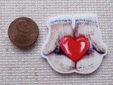 Second view of a pair of mittened hands is holding a red heart minder.