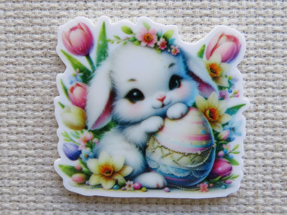 First view of Cute white bunny with an Easter Egg sitting in flowers minder.