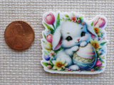 Second view of Cute white bunny with an Easter Egg sitting in flowers minder.