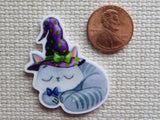 Second view of stripped gray kitten is curled up asleep while wearing a purple witch's hat and a cute purple bow minder.