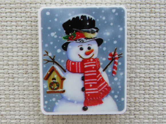 First view of Red scarf wearing snowman with a birdhouse in one hand and a candy cane in the other minder.