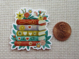 Minder of stacked books with flowers next to a penny.