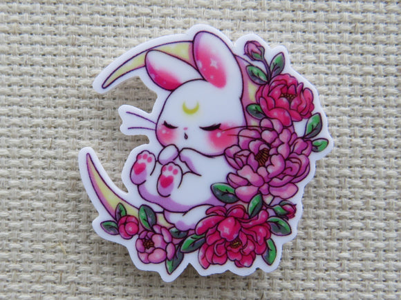 First view of White bunny is sleeping on a bed of red and pink flowers in a crescent moon minder.